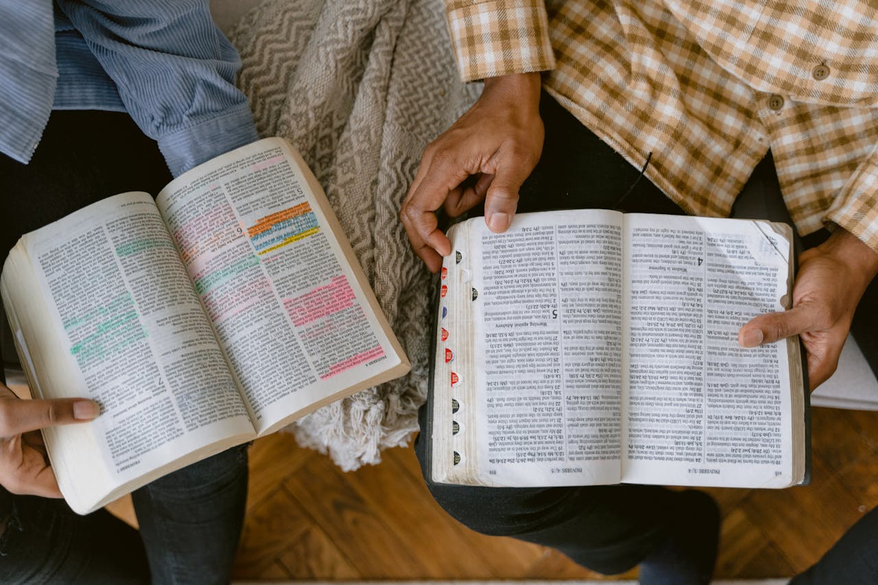 Two adults reading religious texts with highlighted passages indoors, sharing a moment of learning and connection.